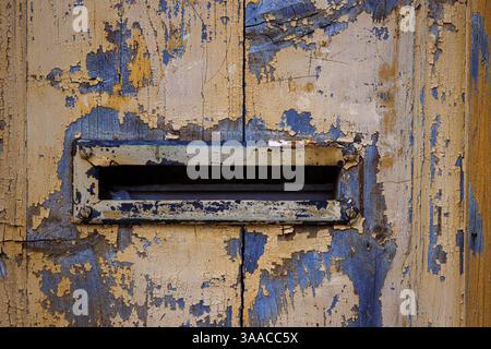 Closeup image of a weathered, peeling paint on an old wooden door with a vintage mail slot, perfect for backgrounds, textures, and rustic-themed desig Stock Photo