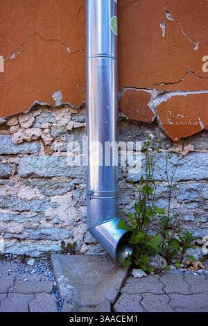 Galvanized metal downspout dreainpipe against an old weathered stone and cracked stucco wall.  ideal for urban decay, architecture, and texture backgr Stock Photo