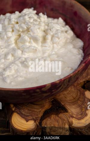 cottage cheese made from milk with cream close-up, grainy cottage cheese with cream on the table, cottage cheese in a wooden bowl, side view Stock Photo