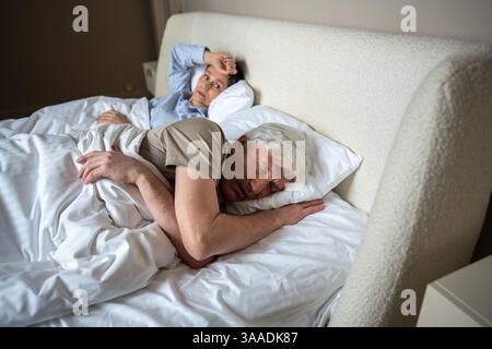 Upset angry wife lies in bed after argument watching husband who fell asleep ignoring conflict Stock Photo