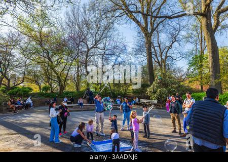 Children playing with giant soap bubbles in spring park during sunny day under adult supervision. New York. USA. Stock Photo
