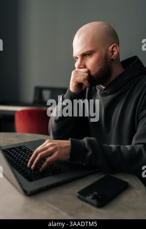 Vertical shot of thoughtful freelancer remote working from home office, sitting at table with laptop computer, contemplating strategies for upcoming Stock Photo