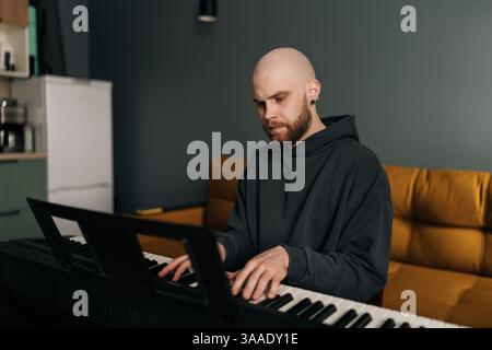 Concentrated male musician plying on electric piano, composing music at home, practicing and recording new song in stylish modern apartment setting. Stock Photo