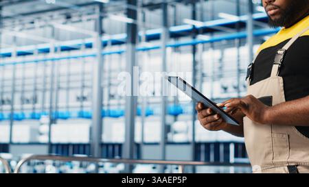 Smart factory expert using digital device app to test automated systems and ensure reliability. Worker uses tablet to identify bottlenecks and optimize gear based on sensors data, camera A close up Stock Photo