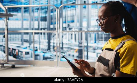 Worker using tablet in smart factory, collecting and analyzing data. Expert using tracking software on device in industry 4.0 industrial plant equipped with advanced sensors, camera A close up Stock Photo