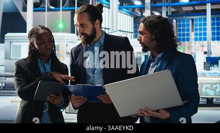 Team of photovoltaics factory engineers working together to improve solar panels efficiency. Teamworking solar panels manufacturing plant experts researching cheaper solar solutions, camera A Stock Photo