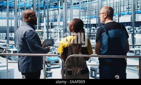 Manager supervising photovoltaic smart factory workers designing production lines in CAD software. Industry 4.0 solar panels plant team leader overseeing employees optimizing floor layouts, camera A Stock Photo