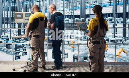 Engineers in industry 4.0 industrial plant controlling automated machinery, ensuring workflow continuity. Technicians in smart factory managing robotic arms and conveyor belts, camera A Stock Photo