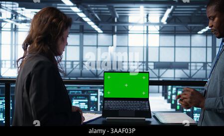 Coworkers in data center using mockup laptop, integrating green technologies. IT experts in server room using chroma key notebook to implement sustainable energy solutions, camera B close up Stock Photo