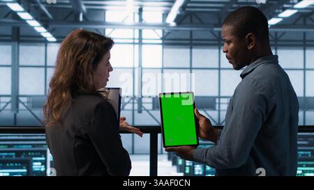 Software developers in data center using mockup tablet, observing performance analytics charts. Server hub IT professionals talking, using chroma key device, looking over graphs, camera A Stock Photo