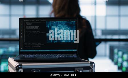 Laptop in front of data center engineers in background deploying artificial intelligence tools. AI coding on notebook screen next to technicians inspecting server clusters, camera A close up Stock Photo