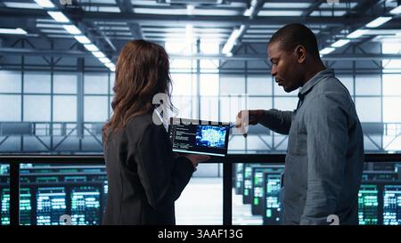 Software developers in data center use AI technology on tablet to optimize storage volumes. IT specialists in server hub facility using artificial intelligence to ensure seamless operations, camera B Stock Photo