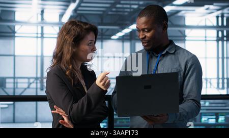 Engineers using laptop in data center, managing server virtualization, running scripts. IT specialists using programming language on notebook in server hub, finetuning network protocols, camera A Stock Photo