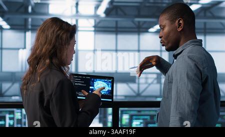 Software developers in data center use AI technology on tablet to optimize storage volumes. IT specialists in server hub facility using artificial intelligence to ensure seamless operations, camera A Stock Photo