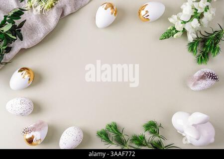 White and golden Easter eggs, Easter Bunny, feathers and greenery on soft background. Top view, flat lay, copy space. Stock Photo