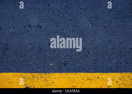 Closeup of a concrete surface featuring a striking yellow stripe on a dark gray asphalt background, ideal for urban, modern, and minimalistic photogra Stock Photo