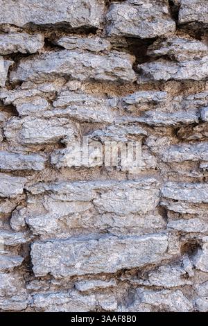 Weathered rough aged gray stone wall texture with rugged, coarse uneven irregular rocks, stacked together, revealing an old historic architectural sty Stock Photo