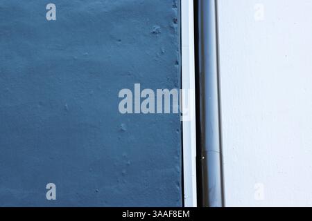 Minimalist wall design with contrasting blue and white surfaces divided by a vertical sleek gray pipe, showcasing clean lines and modern architectural Stock Photo