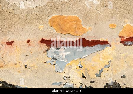 Weathered aged concrete wall with chipped peeling paint layers in earthy tones, including orange, red, and yellow, beige and gray. Distressed and text Stock Photo