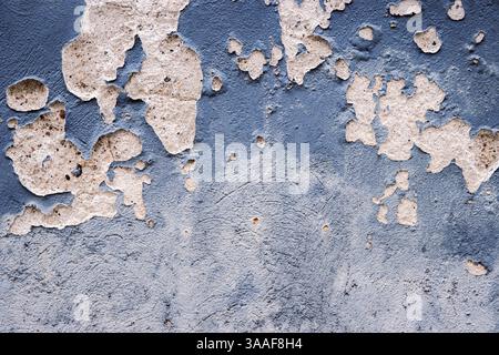 Weathered, peeling blue gray paint on an old concrete wall, revealing underlying bricks. Rough textures, cracks, and faded colors. Copy space Stock Photo