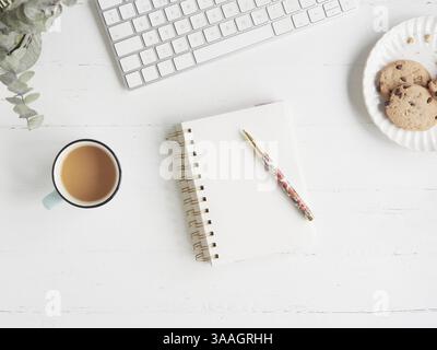 Break and snack in office work. Flat composition with copy space on white desk table with coffee cup and plate of cookies next to notebook and pen nex Stock Photo