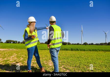 Two engineers are analyzing wind turbines in a green field, working on a project for renewable energy and sustainability Stock Photo