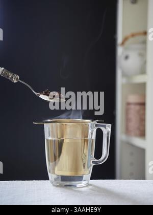 Spoon with roibois red tea on glass cup with steaming hot water with golden metallic filter Stock Photo