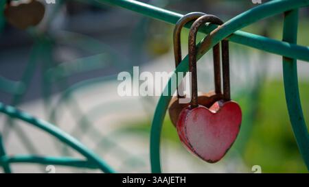 Padlock in shape of red heart hangs on fence. Symbol of eternal love and strong relationships. Stock Photo