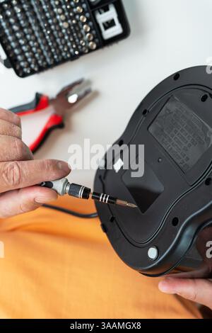 A person carefully repairs a broken appliance using a small screwdriver and other tools, showcasing a detailed close-up of the repair process. Stock Photo