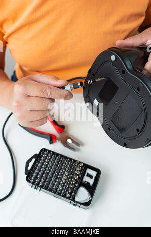 A person meticulously repairs a broken appliance using a small screwdriver and a set of tools. Stock Photo