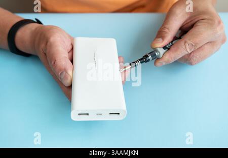 A person repairs a cracked power bank using a small screwdriver. Stock Photo