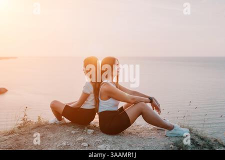 Two Women Sitting on a Cliff at Sunset Stock Photo