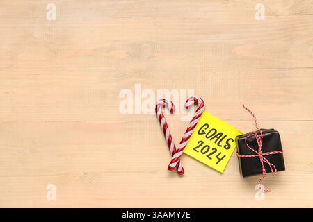 Sticky note with goals for 2024, gift box and candy canes on beige wooden background Stock Photo
