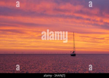 Vibrant sunset with sailing boat anchored in the Baltic Sea off the Falster coast near Gedser, with Rødsand Nysted Wind Farm on the horizon, Denmark Stock Photo