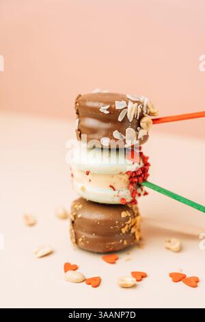 Chocolate french desserts. Cake macaroons on pink background, pastel colors, macaroon decorated with different nuts and hearts, vertical photo. Stock Photo
