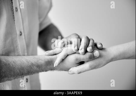 Close up of two hands engaging in delicate touch. Man's and woman's hands on white neutral background. Husband holding hand of his lovely wife. Concept of support, mutual respect. Black and white. Stock Photo