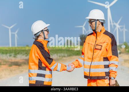 Engineer worker hand shaking team support dealing together at wind turbine energy farm outdoor. Professional modern workers teamwork concept. Stock Photo