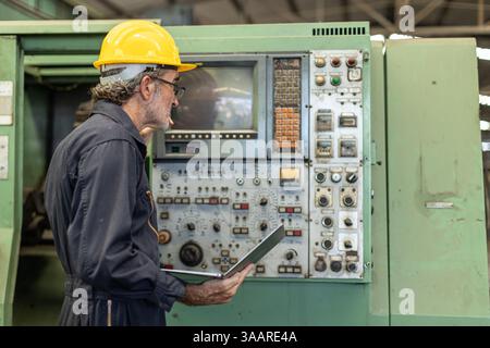 Senior Professional technician engineer male operate control heavy industry machine CNC in factory, Worker pressing machine button. Stock Photo