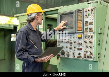 Senior Professional technician engineer male operate control heavy industry machine CNC in factory, Worker pressing machine button. Stock Photo