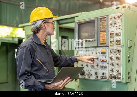Senior Professional technician engineer male operate control heavy industry machine CNC in factory, Worker pressing machine button. Stock Photo