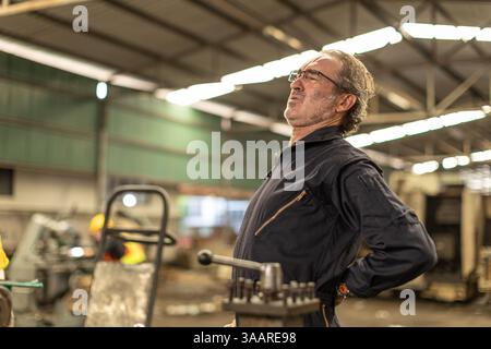 Senior worker tired exhausted muscle pain, Suffer from lower back pain from hard work in heavy industry factory. Stock Photo