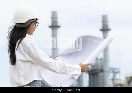 professional smart young engineer women standing against refinery power plant building floor plan. large industry construction project management conc Stock Photo