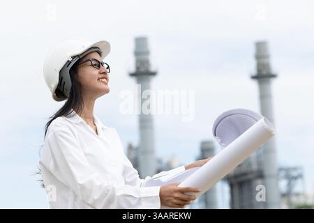 professional smart vision young engineer women standing against refinery power plant building floor plan. large industry construction future project m Stock Photo
