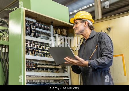Senior Professional Electrician engineer supervisor service maintenance check heavy industry machine electricity wire cable with laptop computer. Stock Photo