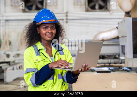 African black women worker with safety suit handle laptop computer program operating machine in wood workshop furniture factory Stock Photo