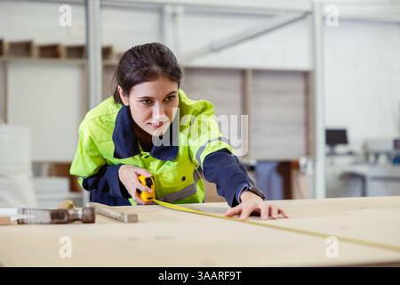 Professional women staff worker enjoy working using ruler tape measure plywood wooden furniture product in factory with safety suit Stock Photo