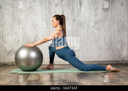 Pregnant woman practicing leg mobility exercise with fitball on yoga mat Stock Photo