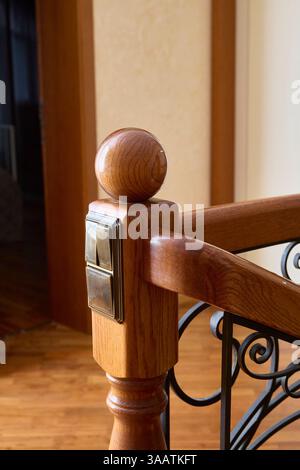 Detailed close-up of a polished wooden staircase post featuring a built-in metallic light switch. The focus is on the craftsmanship of the woodwork an Stock Photo