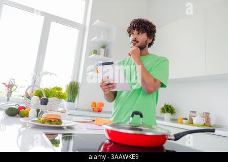Young Man in a Bright Kitchen Using a Tablet to Prepare a Meal while Surrounded by Fresh Ingredients and Daylight Stock Photo