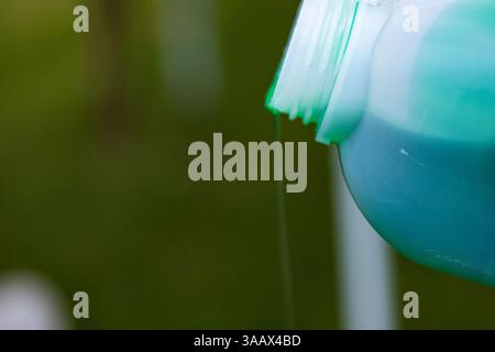 Closeup of vibrant green detergent pouring from a white plastic bottle against a blurred background. Green liquid flowing from a container. Copy space Stock Photo